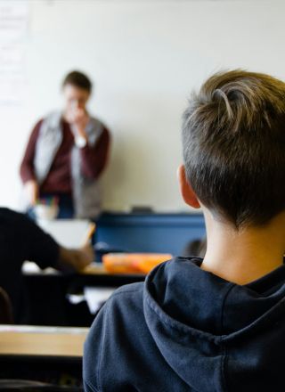 A pupil watching a teacher at the front of a classroom