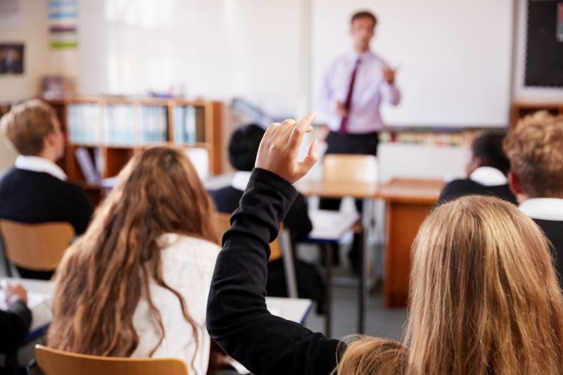 Secondary school pupils in a classroom, one raising a hand