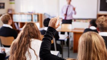 Secondary school pupils in a classroom, one raising a hand