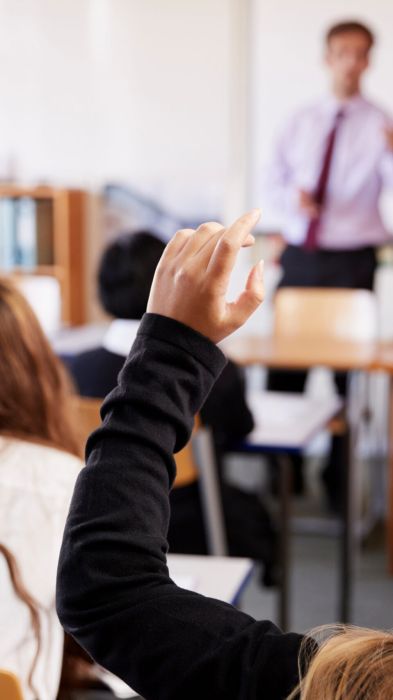 Secondary school pupils in a classroom, one raising a hand