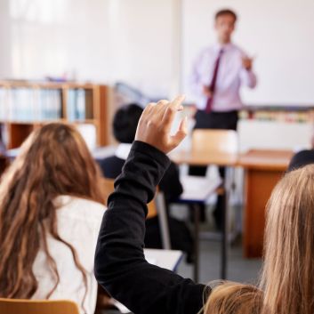 Secondary school pupils in a classroom, one raising a hand